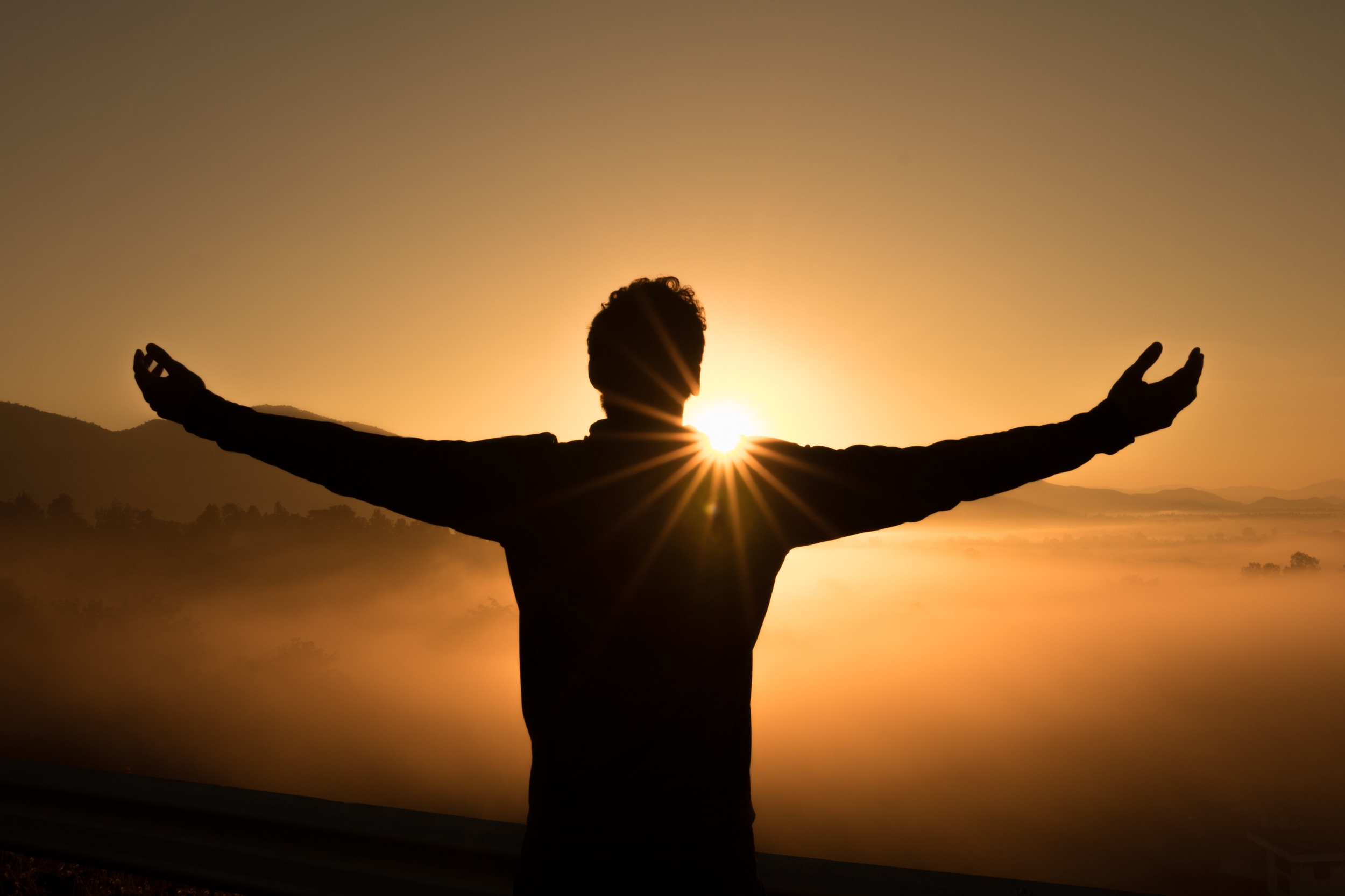 man standing with arms wide open looking at a sunset, representing how to manifest a job using law of attraction