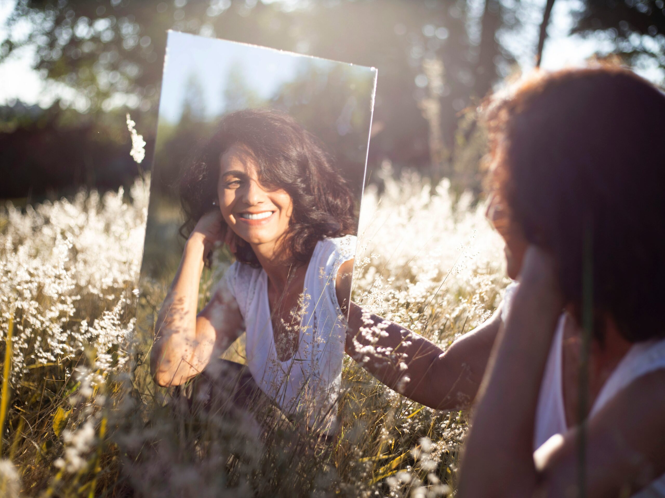 a woman looking at herself in the mirror and smiling, siting in a field, used for article tips for productivity