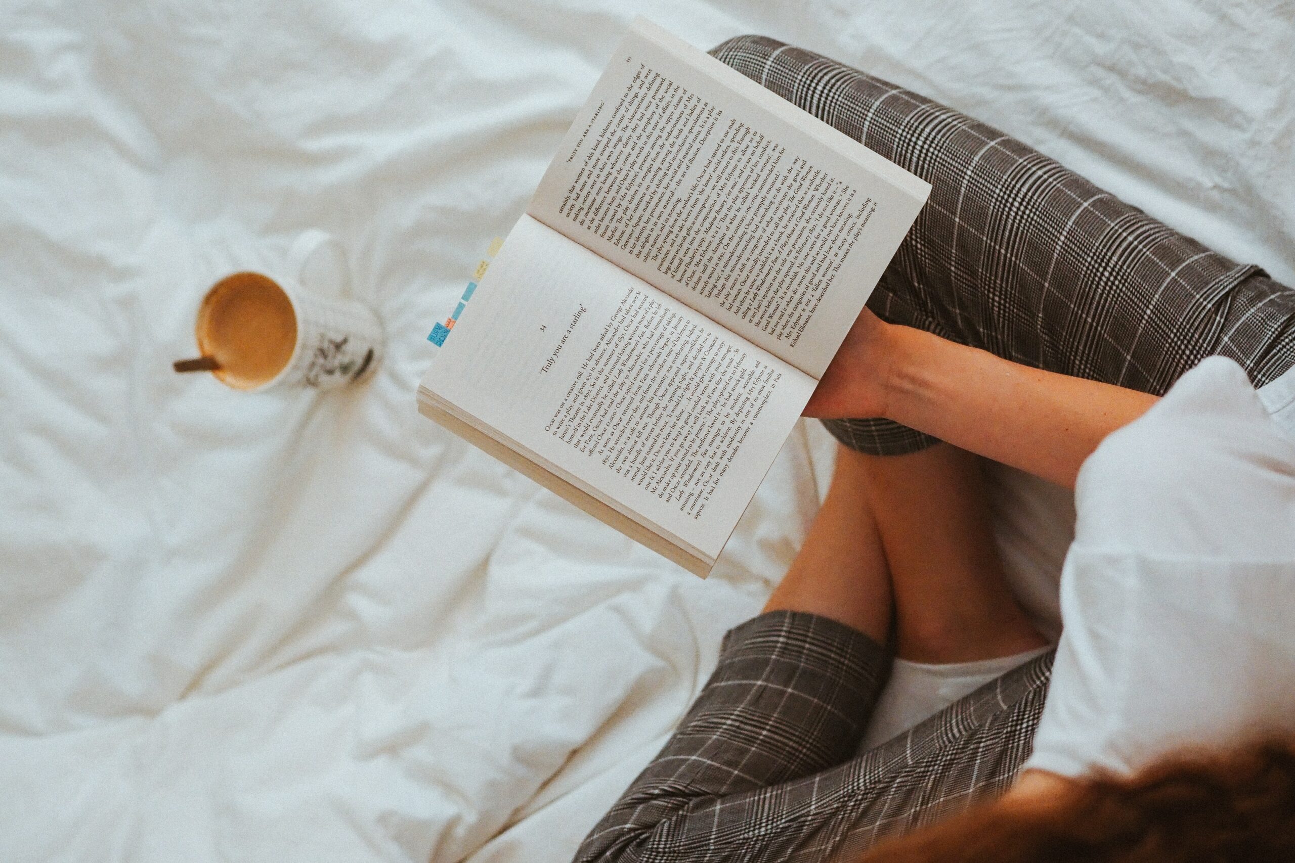 a woman sitting on the bed reading a book with a cup of coffee used for article 10 emotional healing books