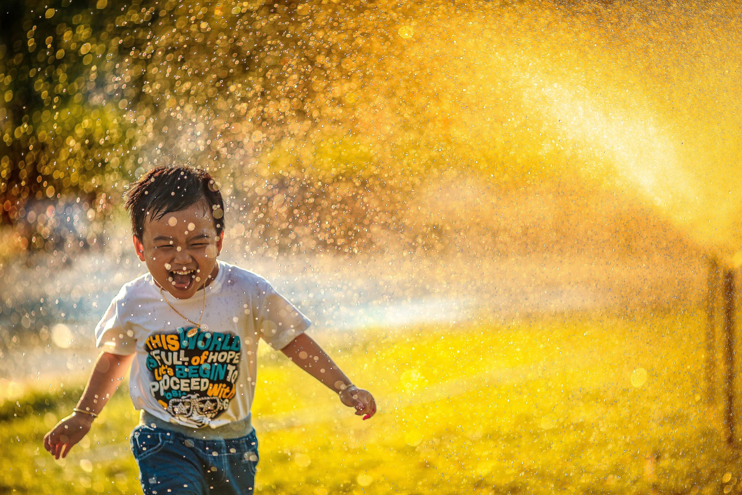 small child running through sprinklers with smile on his face picture used for article 15 inner child journaling prompts